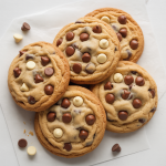 A batch of Big, Fat, Chewy Multichip Cookies photographed from above on a clean white surface. The cookies are thick, golden-brown with slightly cracked tops, packed with multiple chocolate chips (dark, milk, and white). A few extra chips scattered around for detail. Hyper-real texture showing soft centers and crisp edges. Bright white background, evenly lit, no warm tones, no shadows, clean homemade presentation.